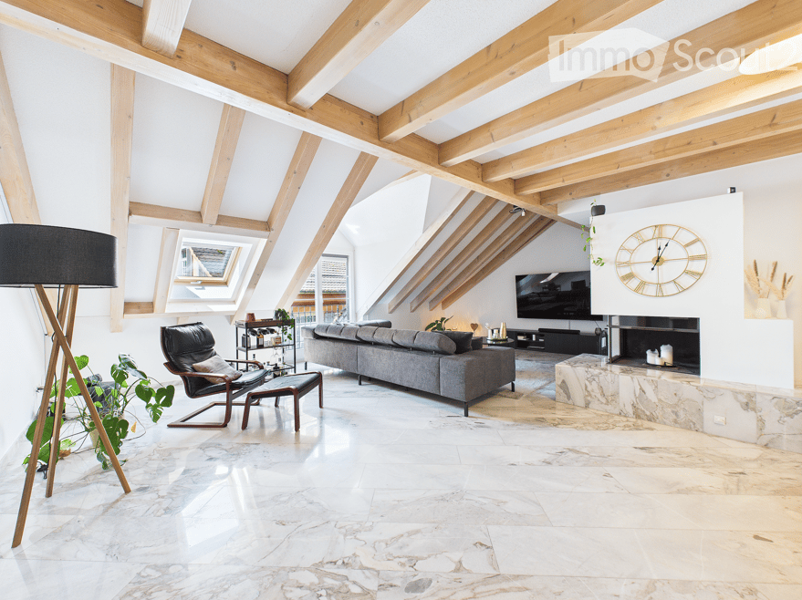 Modern living room with exposed wooden beams, large windows, grey sofa, armchair, coffee table, floor lamp, television, fireplace, and decorative clock.