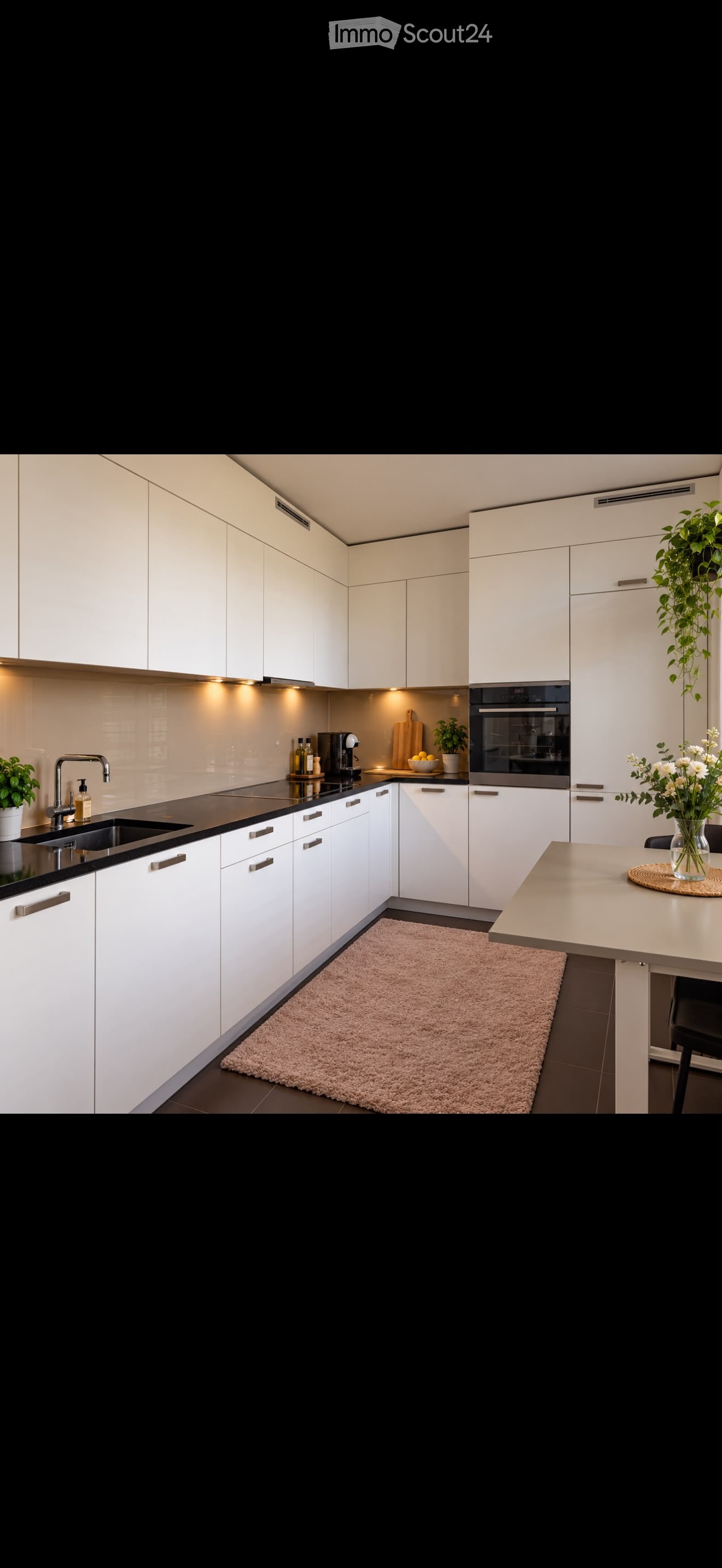 Modern kitchen with white cabinets, black countertops, stainless steel sink, built-in oven, coffee maker, and decorative plants.