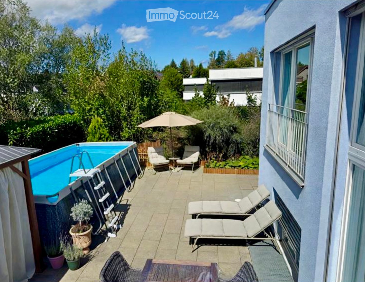 Balcony area with a swimming pool, lounge chairs, umbrella, small table, and potted plants.