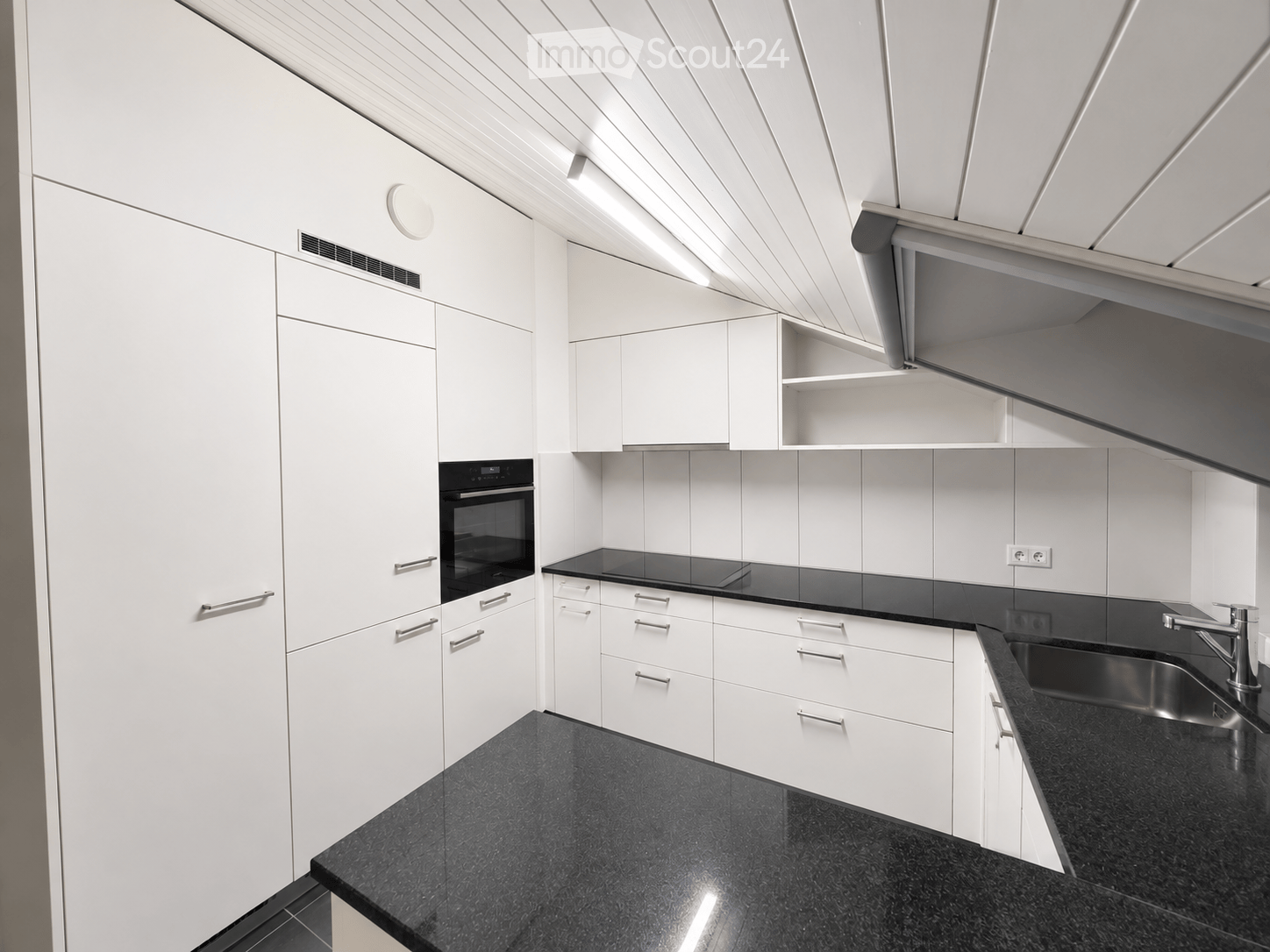 Modern kitchen with white cabinets, black countertops, stainless steel sink, and built-in oven.