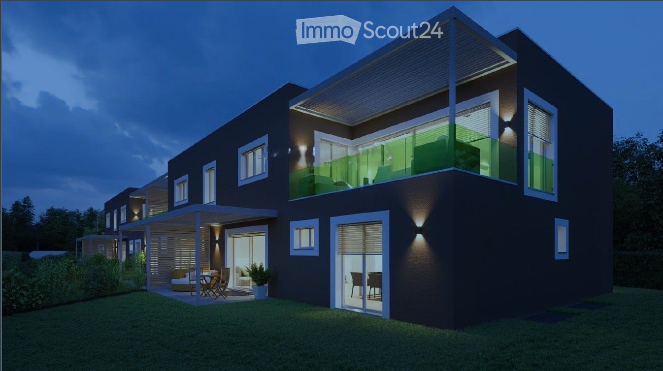 Modern two-story house with dark exterior, large windows, and a balcony on the upper level. The ground floor features a covered patio area with outdoor furniture.