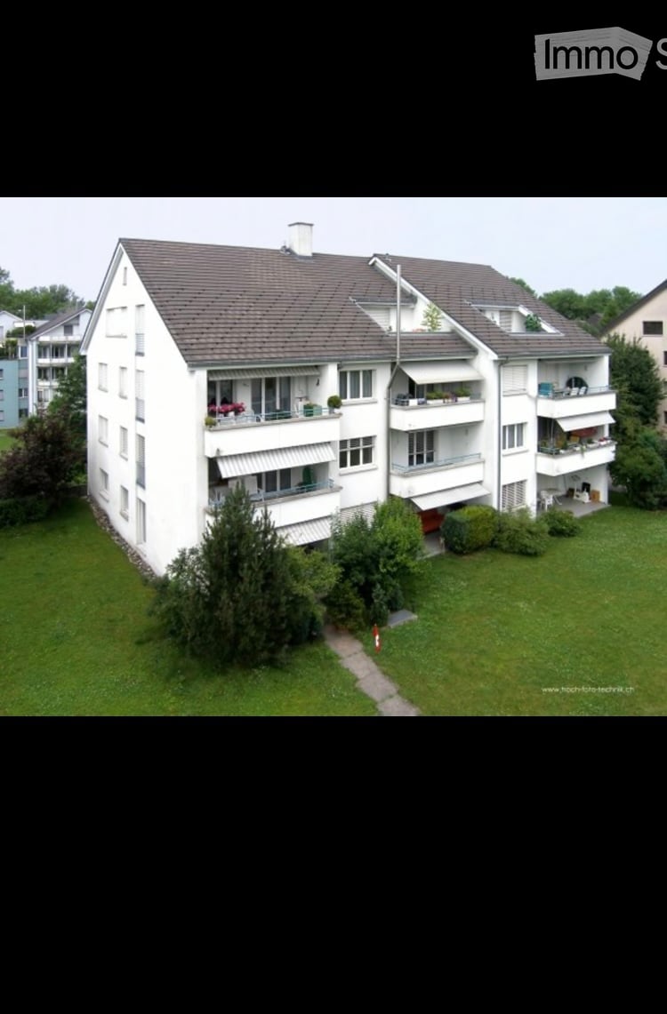 A multi-story residential building with multiple balconies, surrounded by greenery and a well-maintained lawn.