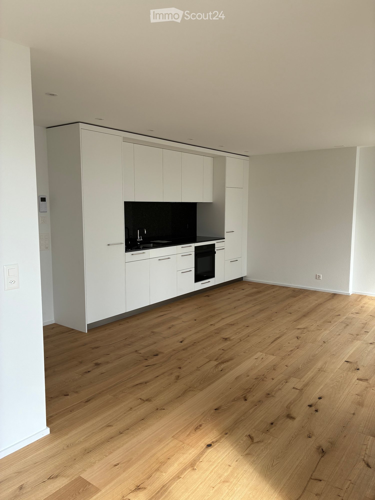 Empty kitchen with white cabinets, a black countertop, and light wooden flooring.
