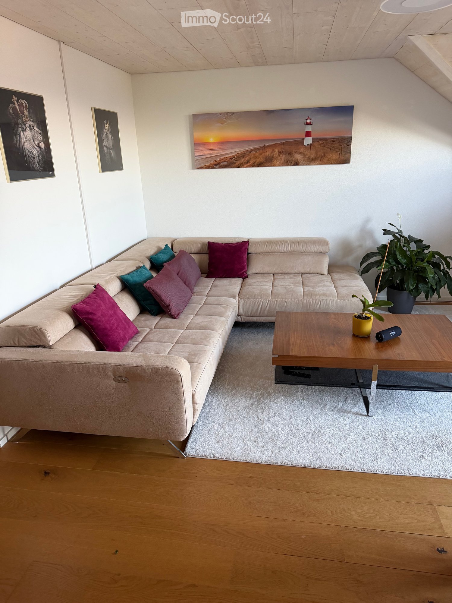 Modern living room with a beige sectional sofa, colorful throw pillows, a wooden coffee table, and a large painting of a lighthouse on the wall.