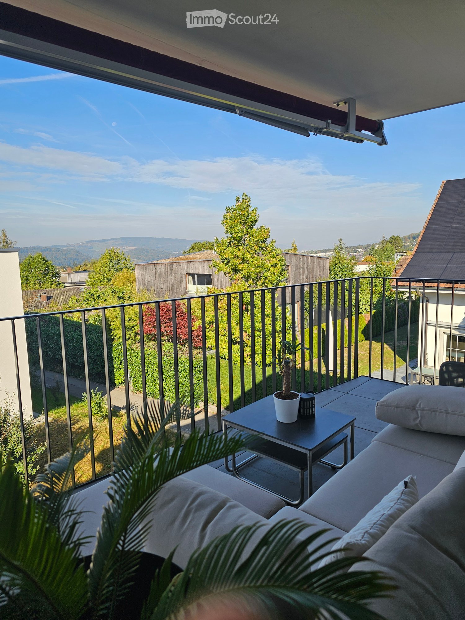 Balcony with a view of the landscape, featuring a sofa, a small table with a potted plant, and cushions.