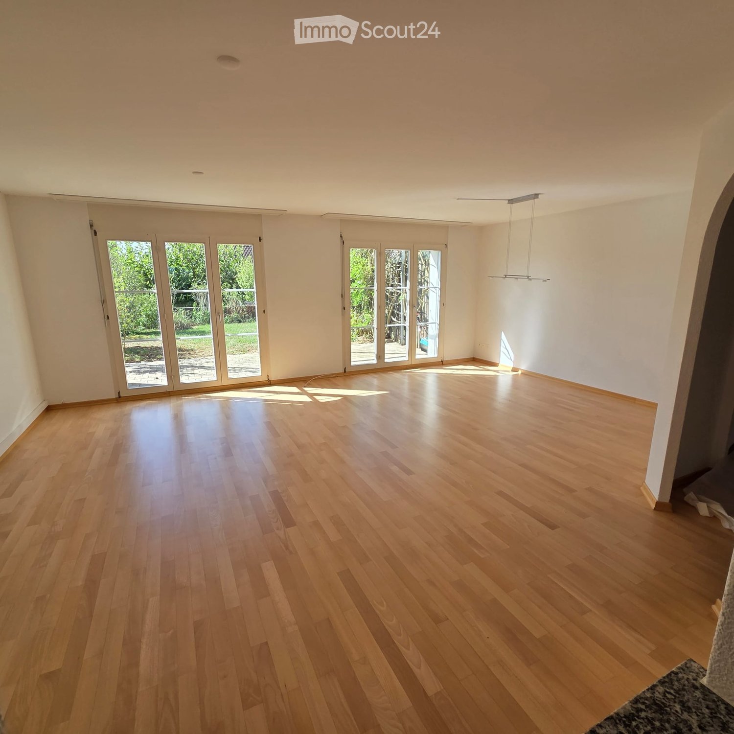Empty room with light wooden flooring, white walls, and large glass doors leading to an outdoor area.