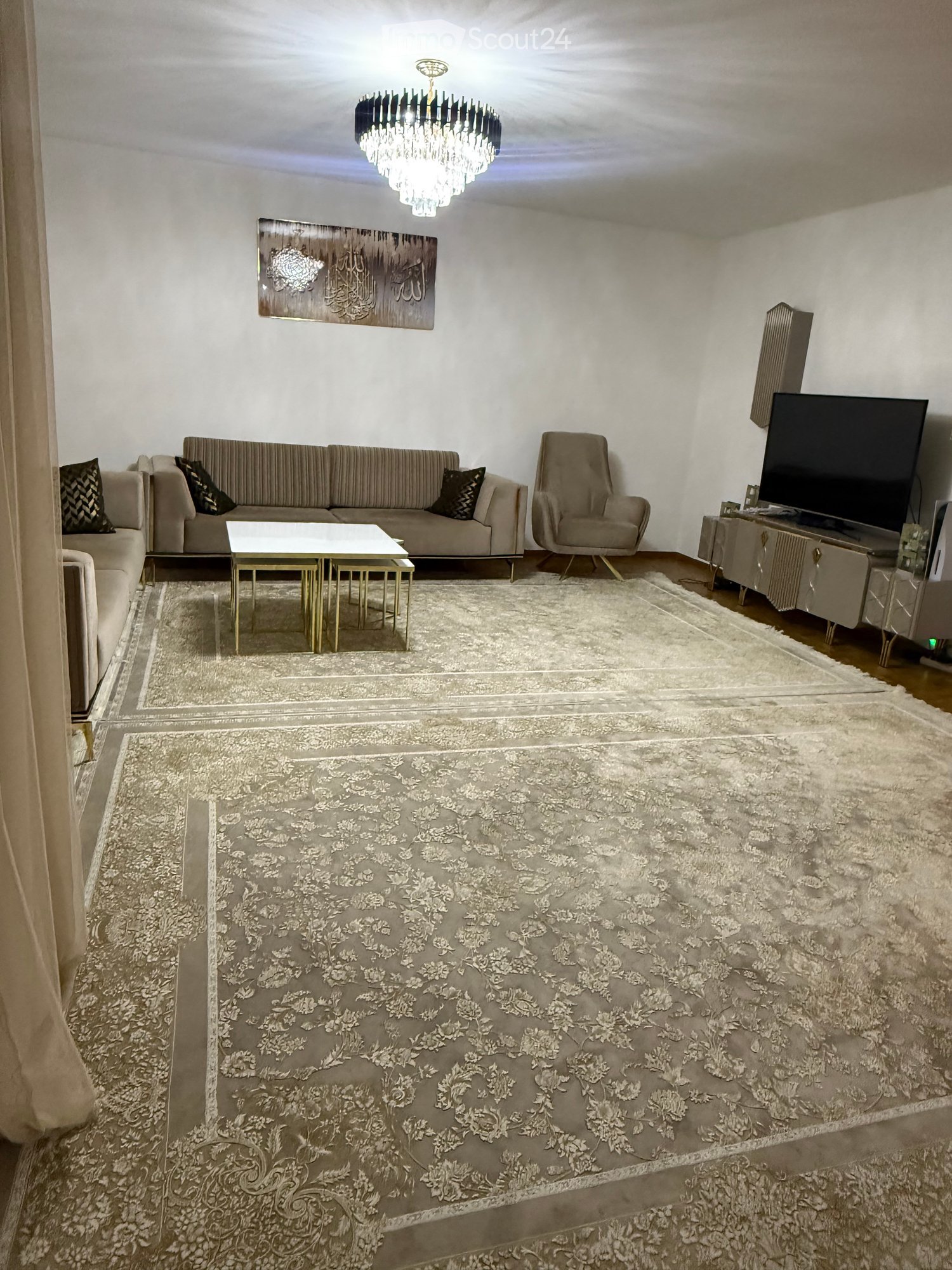 Modern living room with a grey sofa, coffee table, armchair, television, chandelier, and decorative wall art.