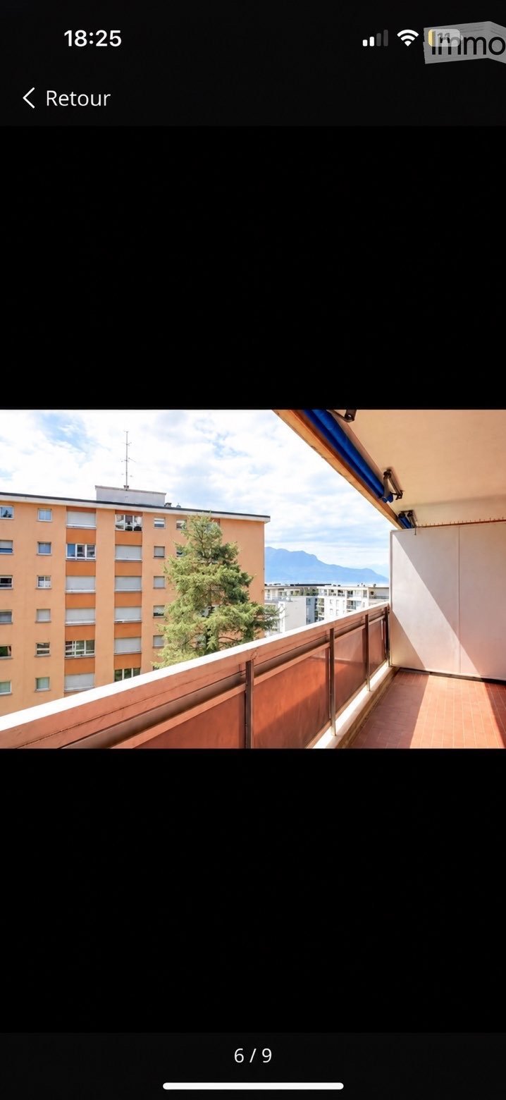 Balcony with wooden flooring, metal railing, and a view of a tree, building, and mountains.