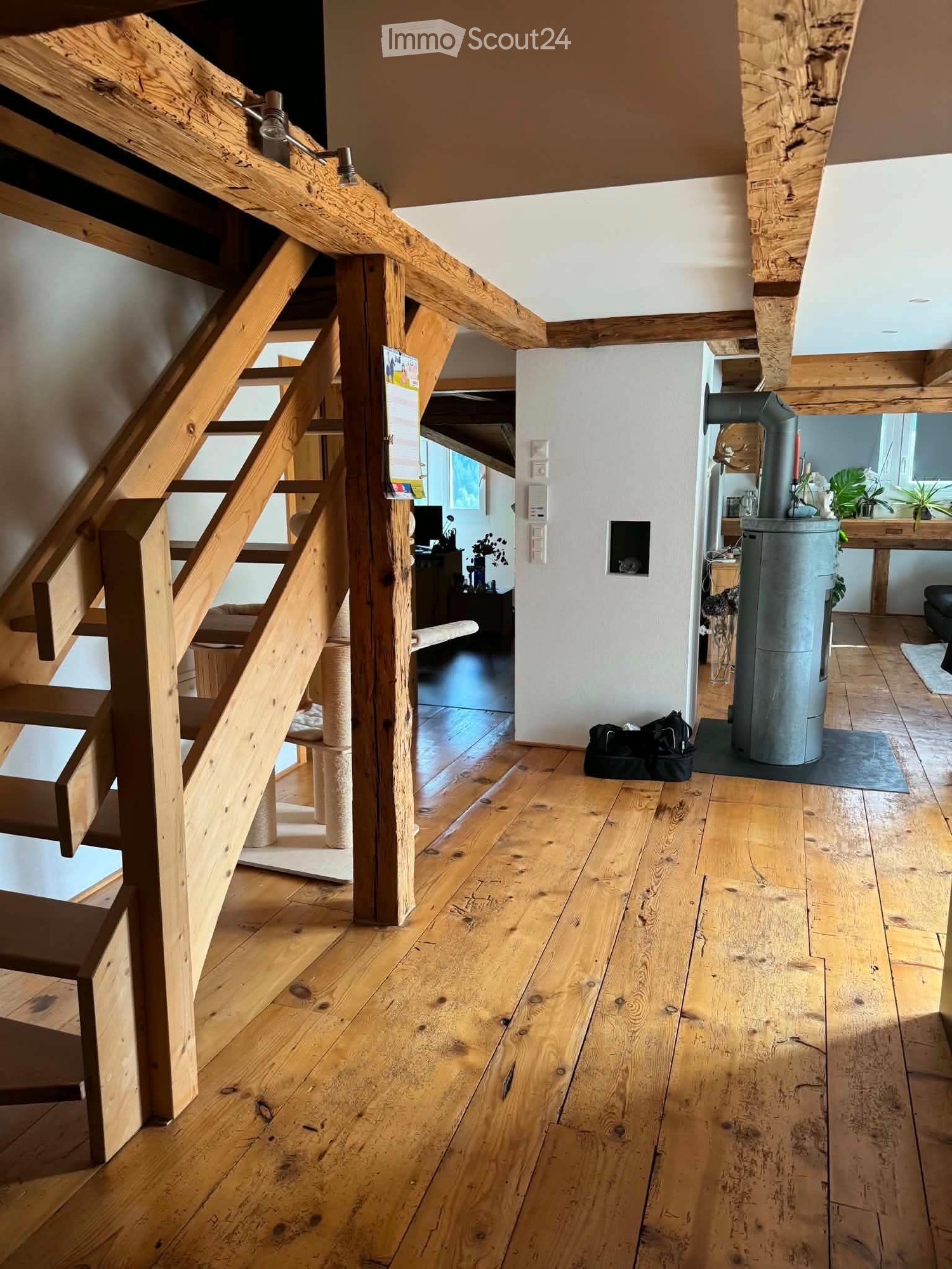 Wooden staircase with exposed beams, wooden floor, and a modern wood-burning stove in the background.