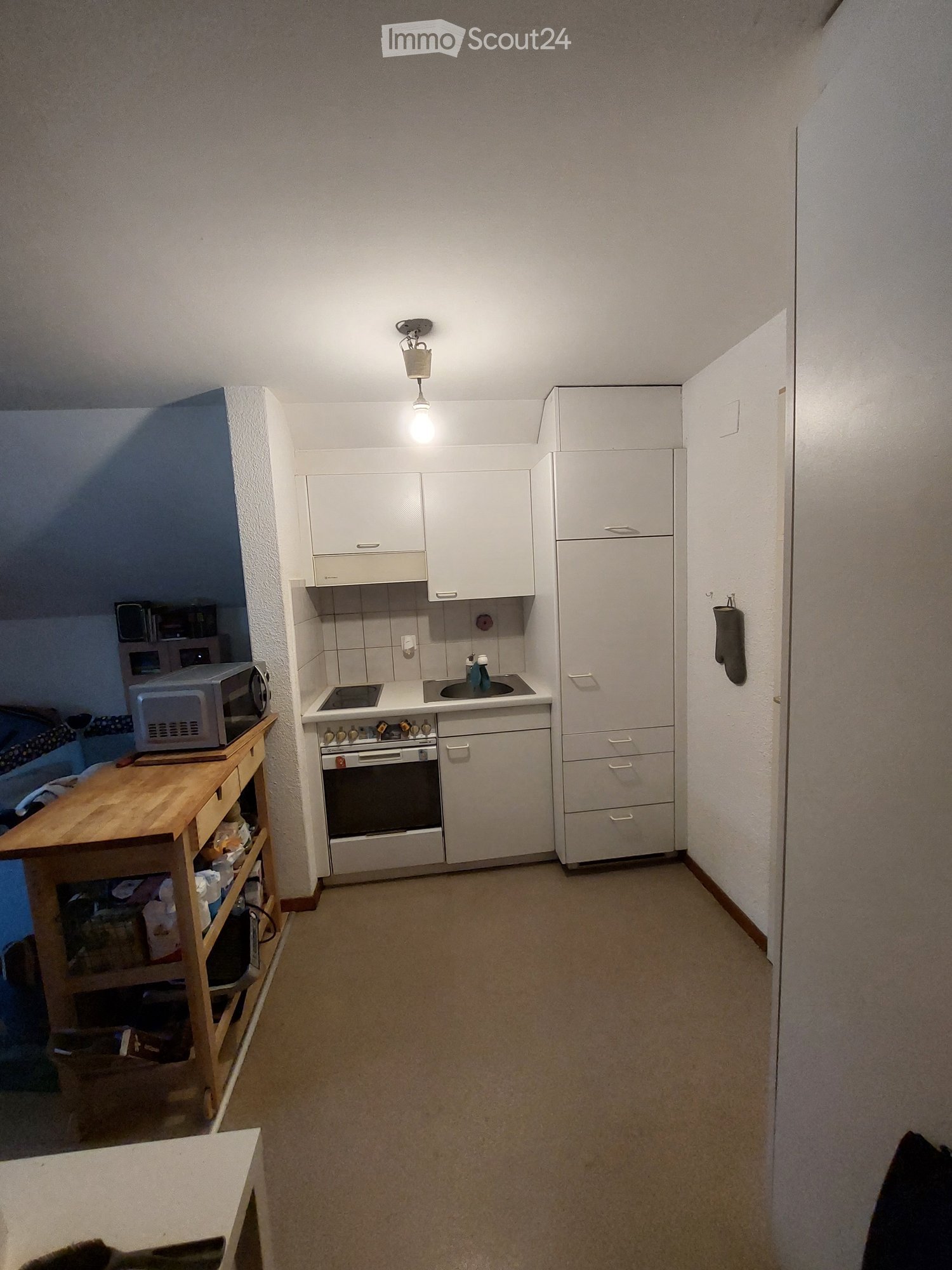 Compact kitchen with white cabinets, a refrigerator, an oven, a sink, and a microwave on a wooden table.