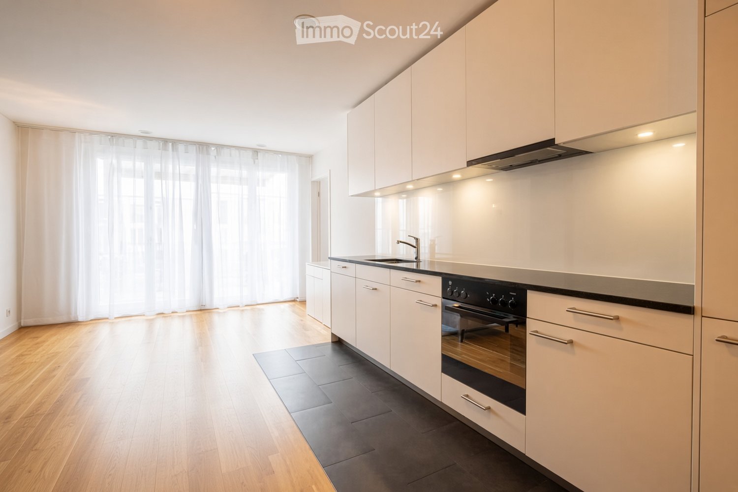 Modern kitchen with white cabinets, wooden flooring, and stainless steel appliances including a sink, faucet, and oven.