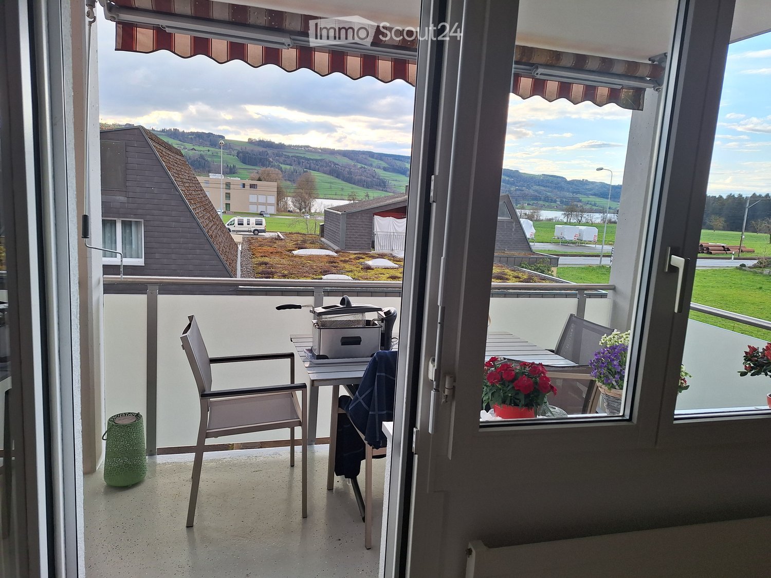 Balcony with a view of a green landscape, featuring a chair, table, and flower pots.
