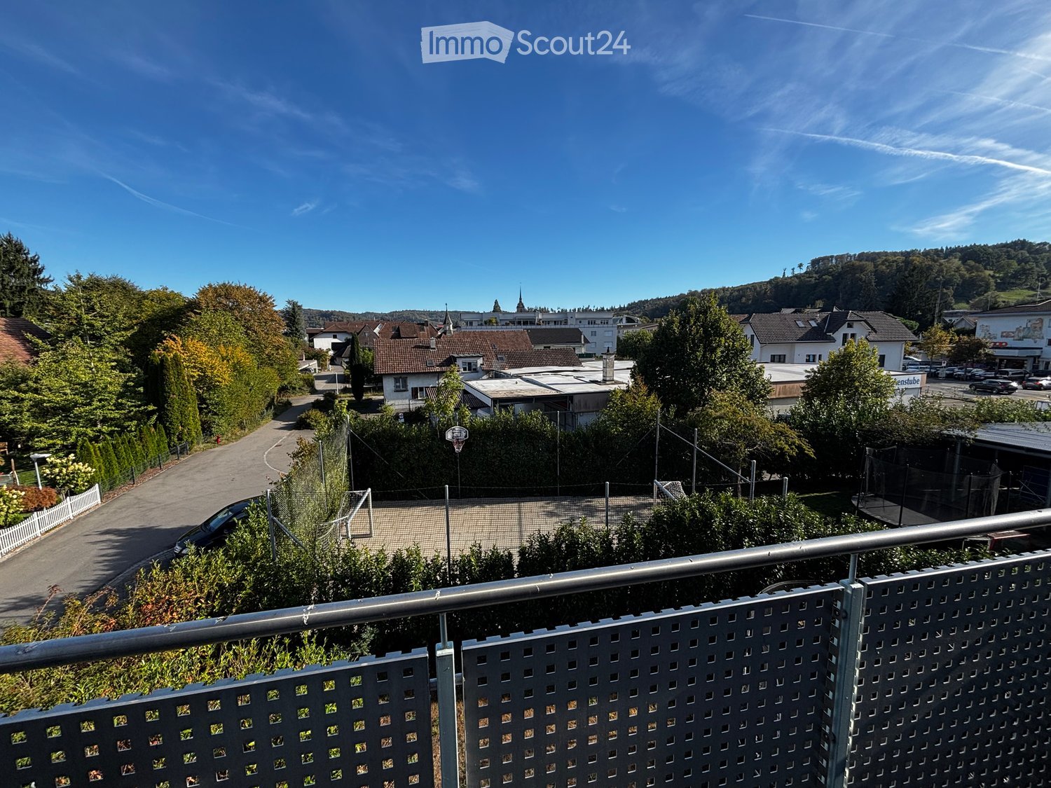 Balcony overlooking a residential area with houses, trees, and a clear blue sky.
