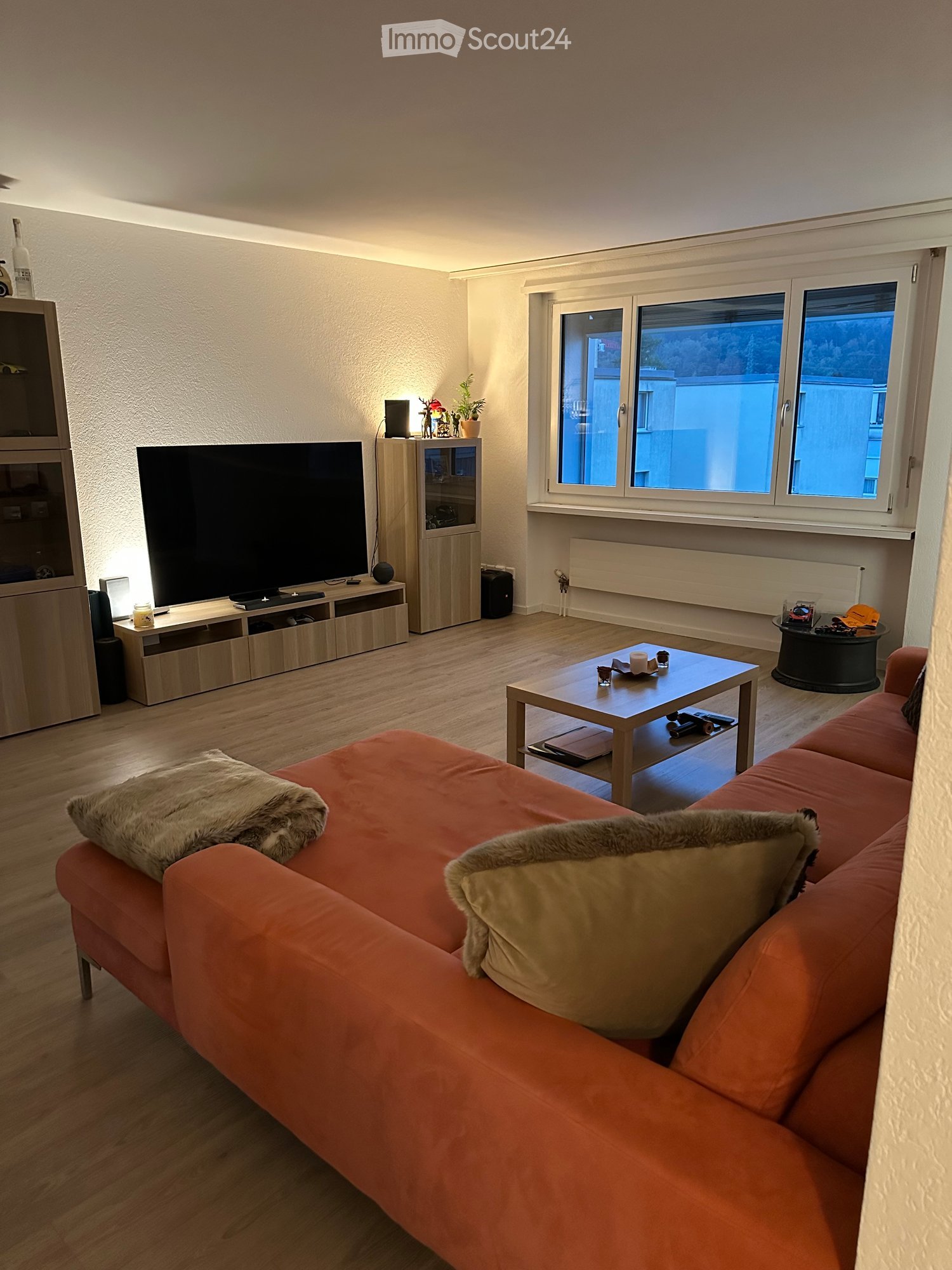 Modern living room with a red sofa, coffee table, TV, and large windows offering a view.