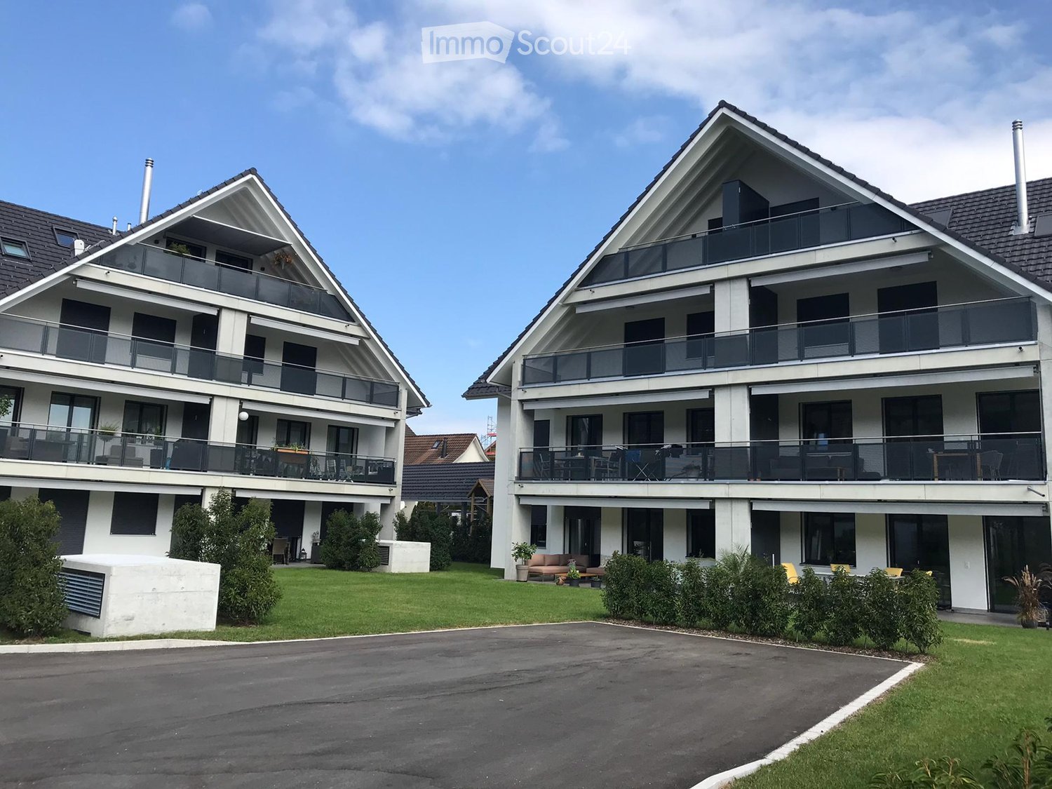 Two-story modern apartment building with white exterior, large balconies, and a well-maintained lawn.