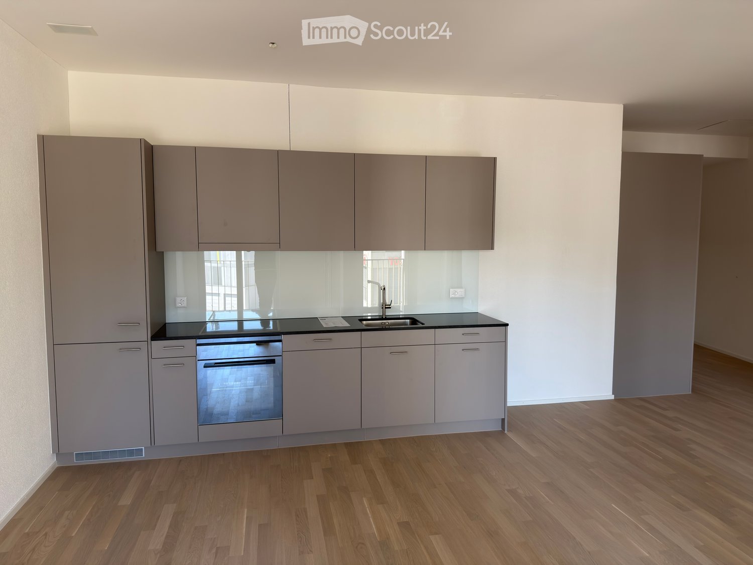 Modern kitchen with grey cabinets, a black countertop, a sink, and an oven. The floor is wooden.