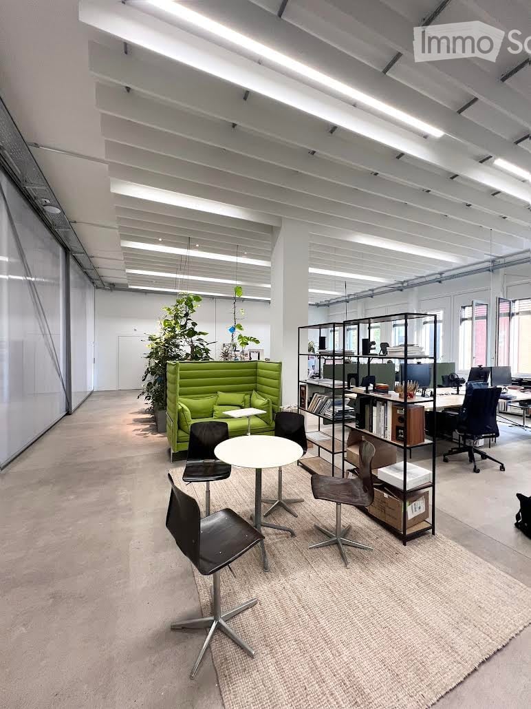 Modern office space with a green sofa, white round table, black chairs, shelving units, and multiple computer screens.