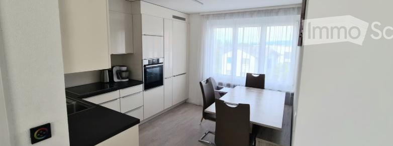 Modern kitchen and dining area with white cabinets, black countertop, built-in oven, coffee maker, and a dining table with four chairs.