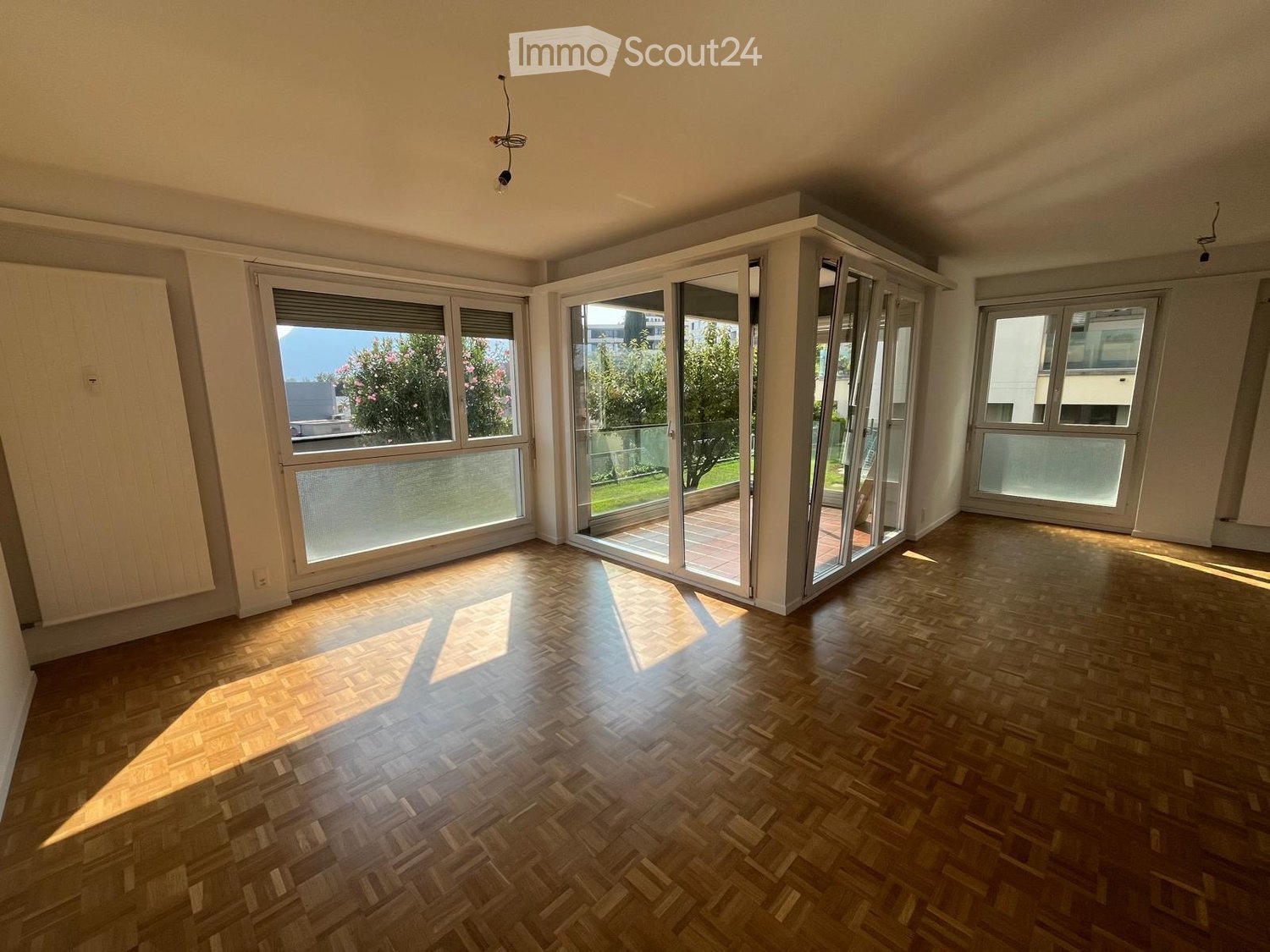 Empty room with wooden parquet flooring, large windows, and sliding glass doors leading to a balcony or terrace area.