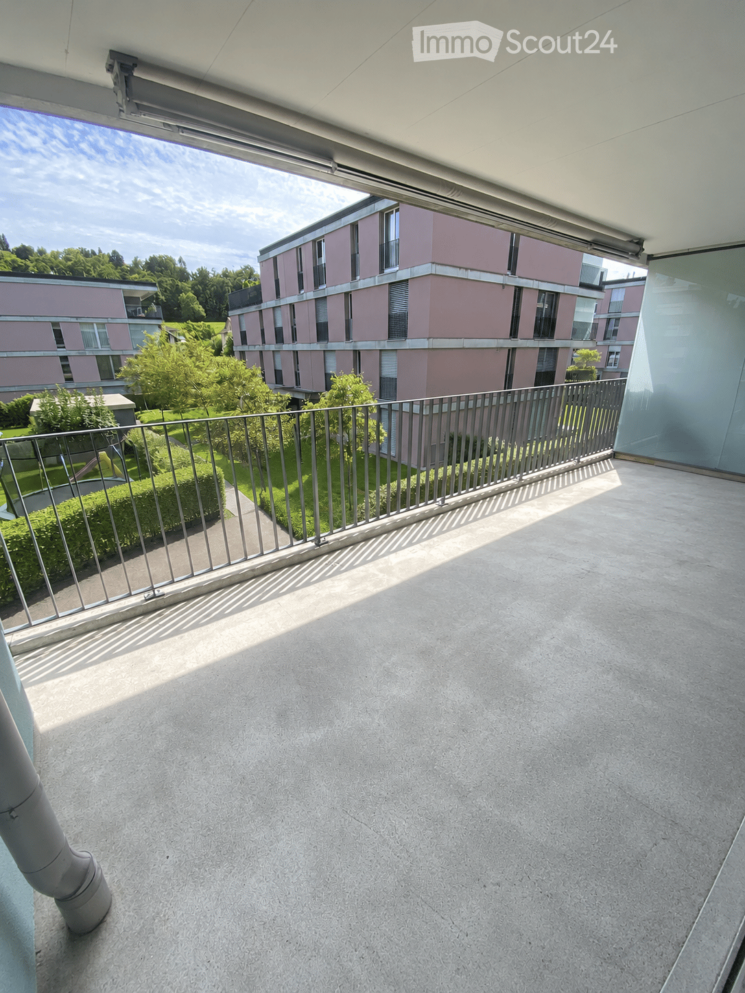 Balcony with modern railing, concrete floor, and view of a residential building and greenery.