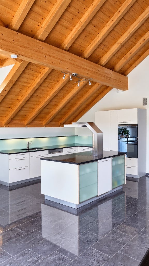 Modern kitchen with white cabinets, black countertops, and a central island. Features a sleek design with stainless steel appliances and a wooden ceiling.
