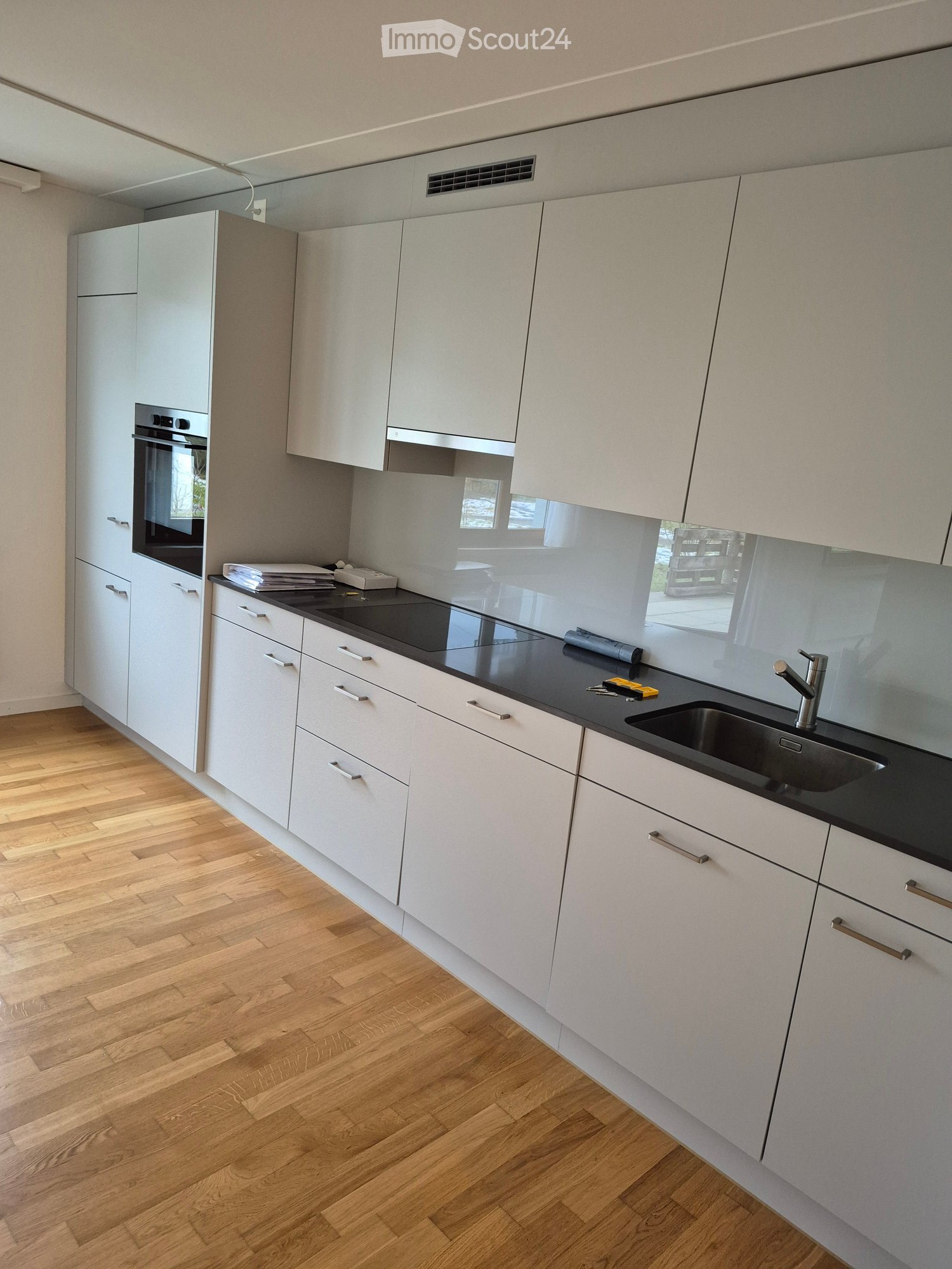 Modern kitchen with white cabinets, black countertop, stainless steel sink, and built-in oven. Wooden flooring and sleek design.