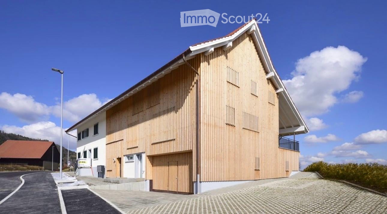 Modern two-story building with a wooden facade and white trim, featuring a garage and a balcony on the upper level.