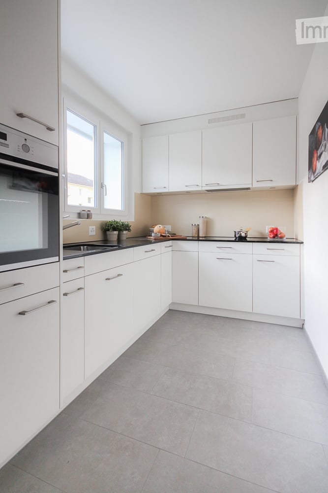 Modern kitchen with white cabinets, stainless steel appliances, and a black countertop. Features include a built-in oven, a sink with a modern faucet, and a small potted plant on the counter.