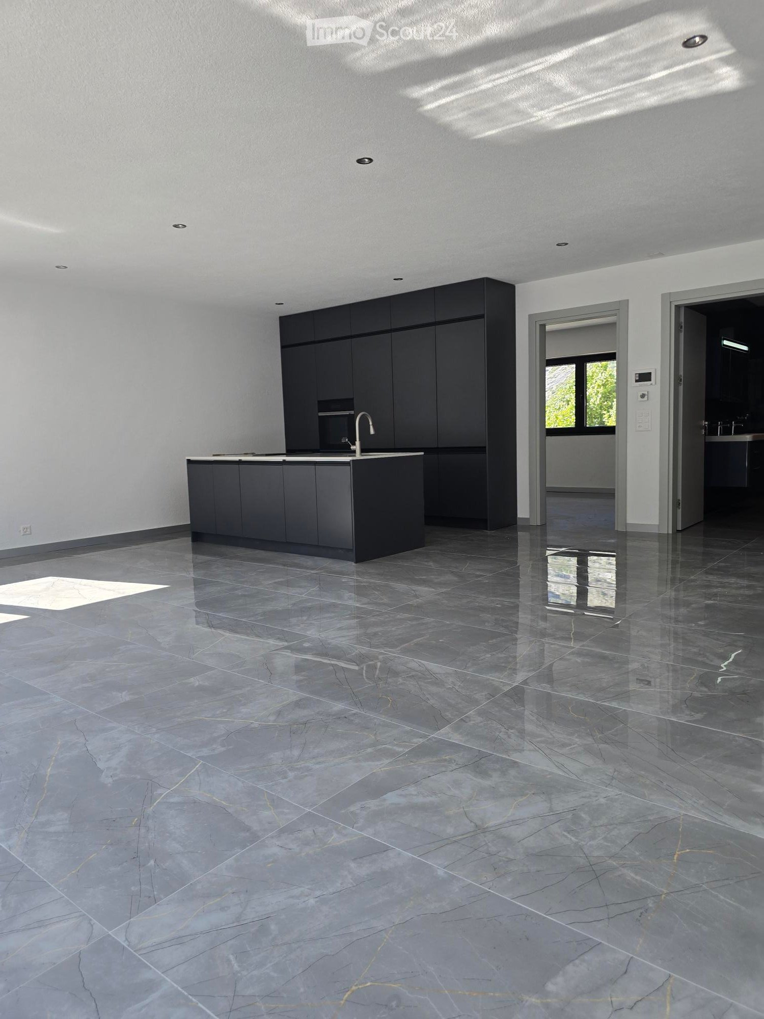 Modern kitchen with dark grey cabinets, a central island, and a polished marble floor. The space is well-lit with recessed lighting and features a sleek, minimalist design.