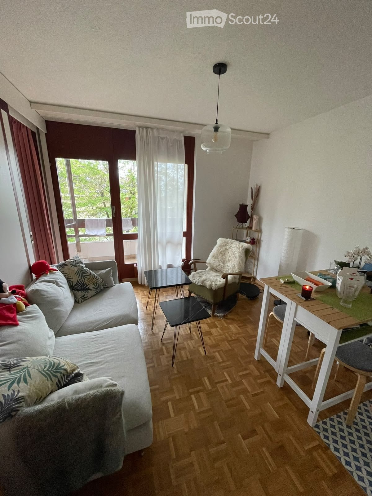 A modern living room with a grey sofa, wooden floor, a small table, and a balcony view.