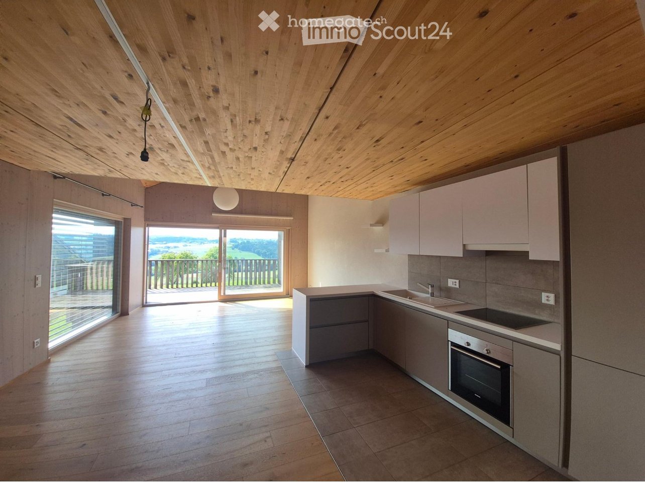 Modern kitchen with light wood flooring, white cabinets, stainless steel appliances, and large windows offering a scenic view.