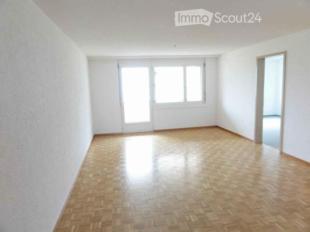 Empty room with wooden parquet flooring, white walls, large windows, and a sliding glass door leading outside.