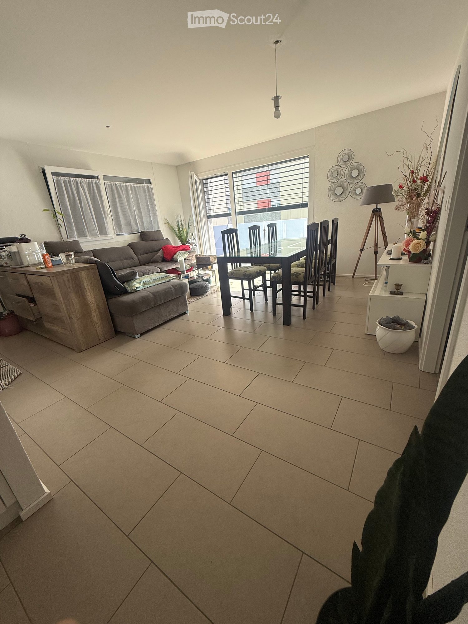 Living and dining area with a grey sectional sofa, dining table with chairs, side table with lamp, and decorative items.