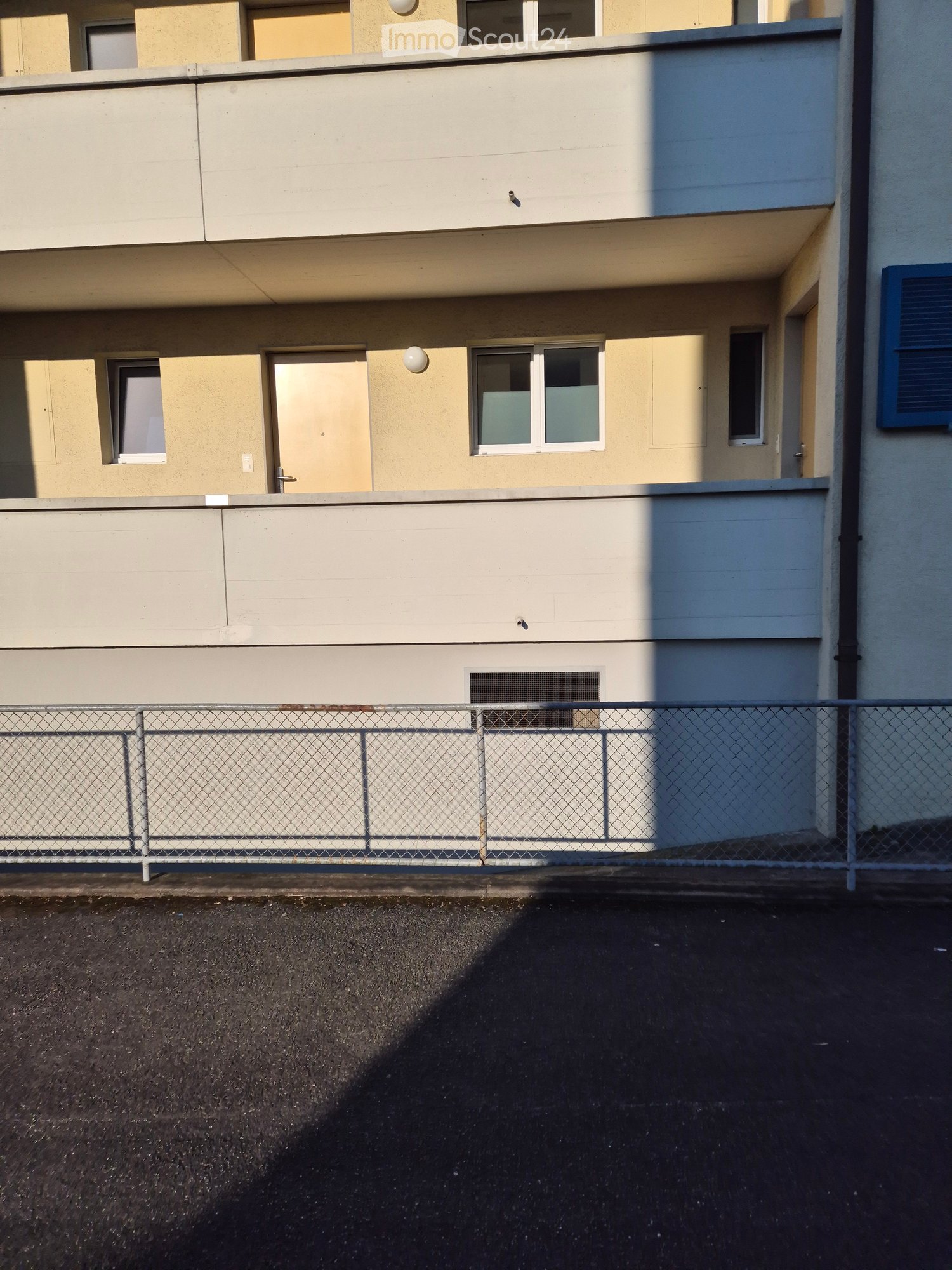 Two-story building with beige walls, multiple windows, and a metal fence in front.