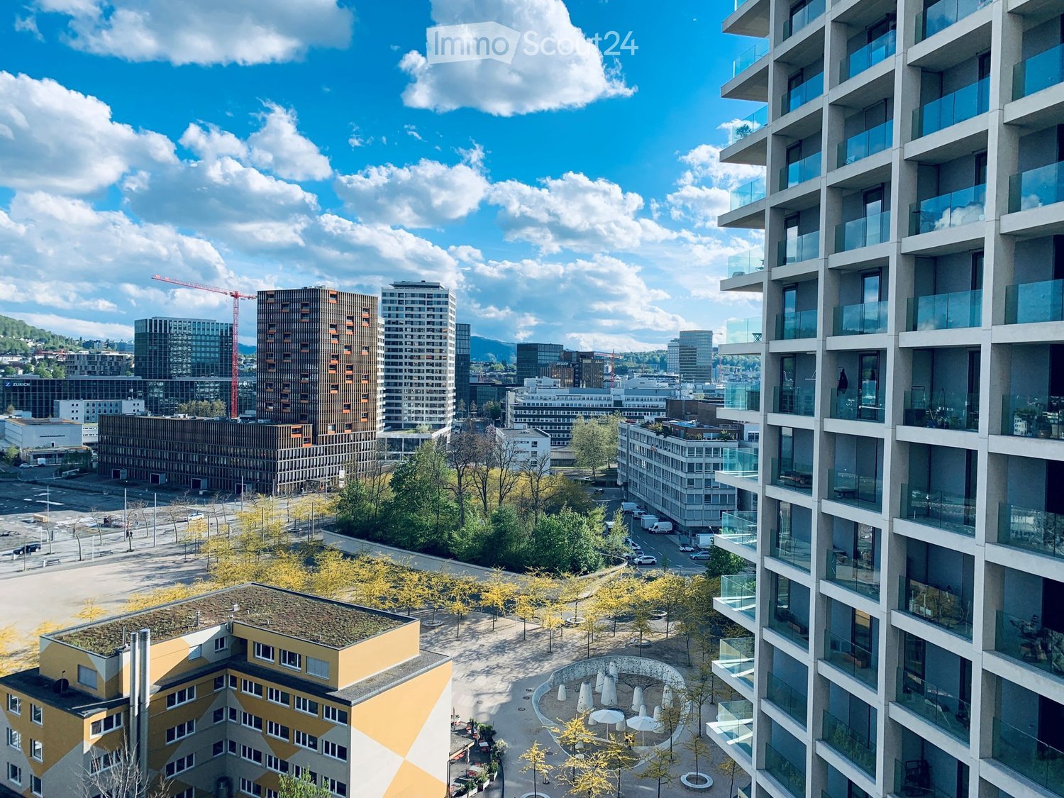 A modern urban skyline with high-rise buildings, balconies, and a green courtyard area with trees and seating.