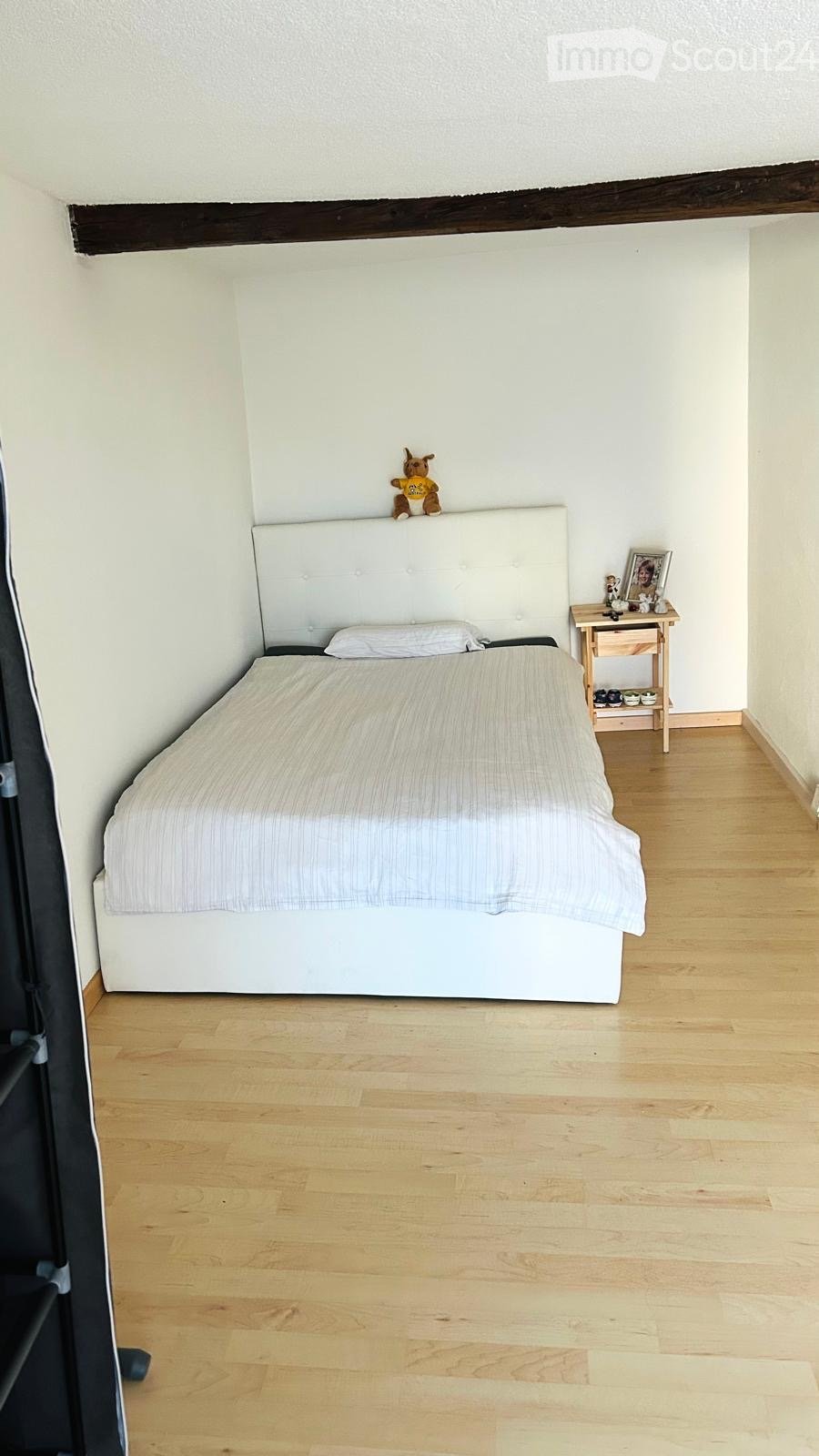 A small, neatly furnished bedroom with a single bed, a nightstand, and a toy on the headboard.