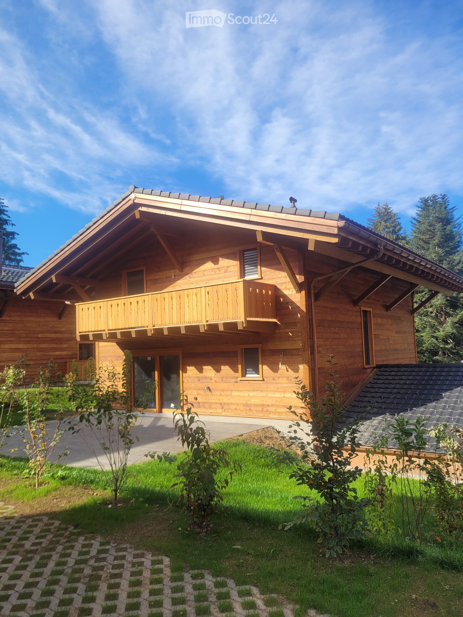 A two-story wooden house with a balcony, large windows, and a well-maintained lawn.