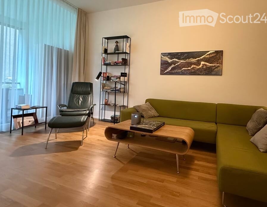 Modern living room with a green sectional sofa, wooden coffee table, black leather chair, bookshelf, and large windows with curtains.