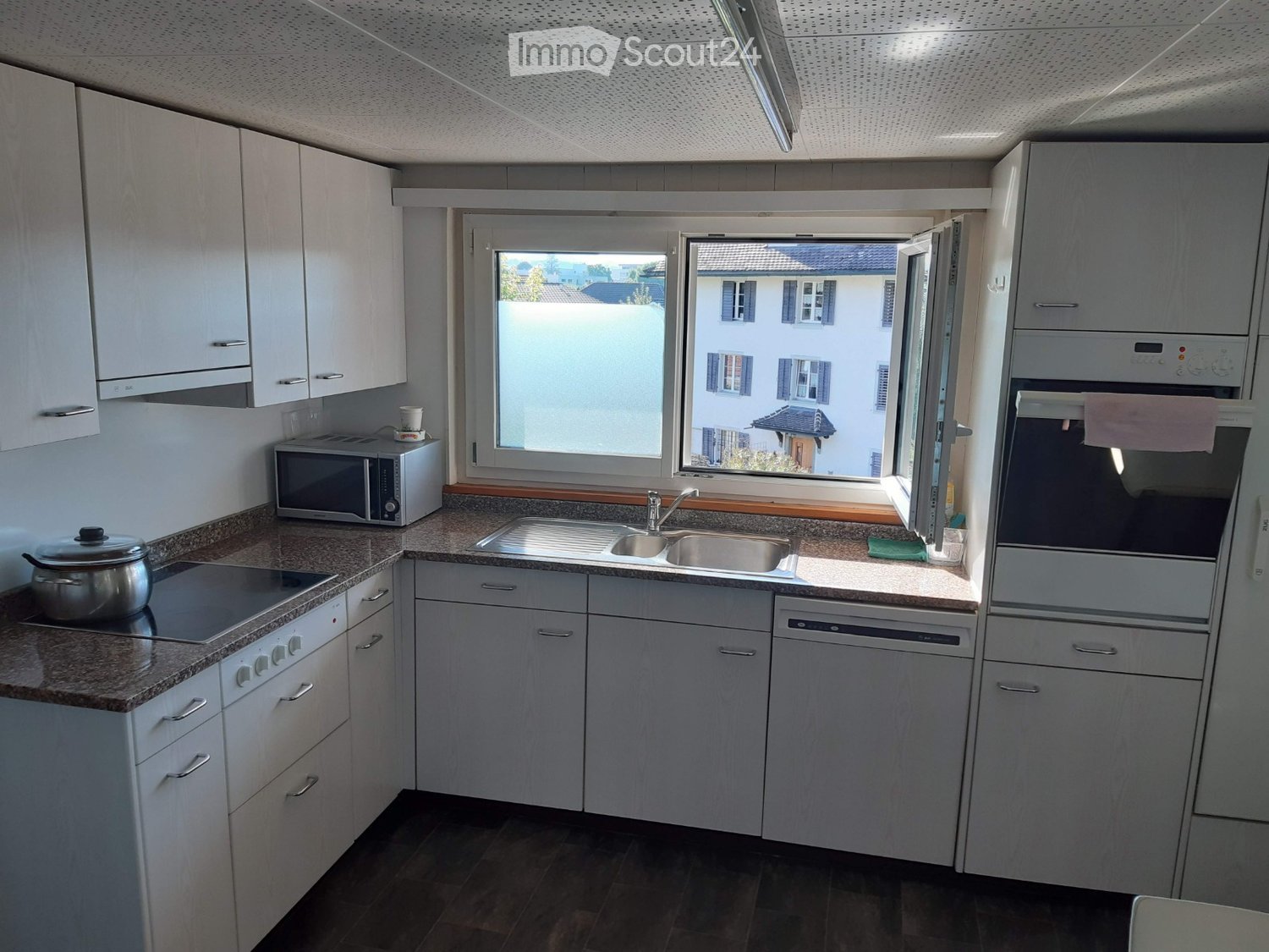 Modern kitchen with white cabinets, granite countertops, stainless steel appliances, and a large window overlooking a residential area.