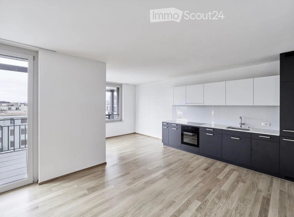 Modern kitchen with light grey cabinets, dark grey lower units, a sink, and an oven. The space features wooden flooring and large windows with a balcony view.