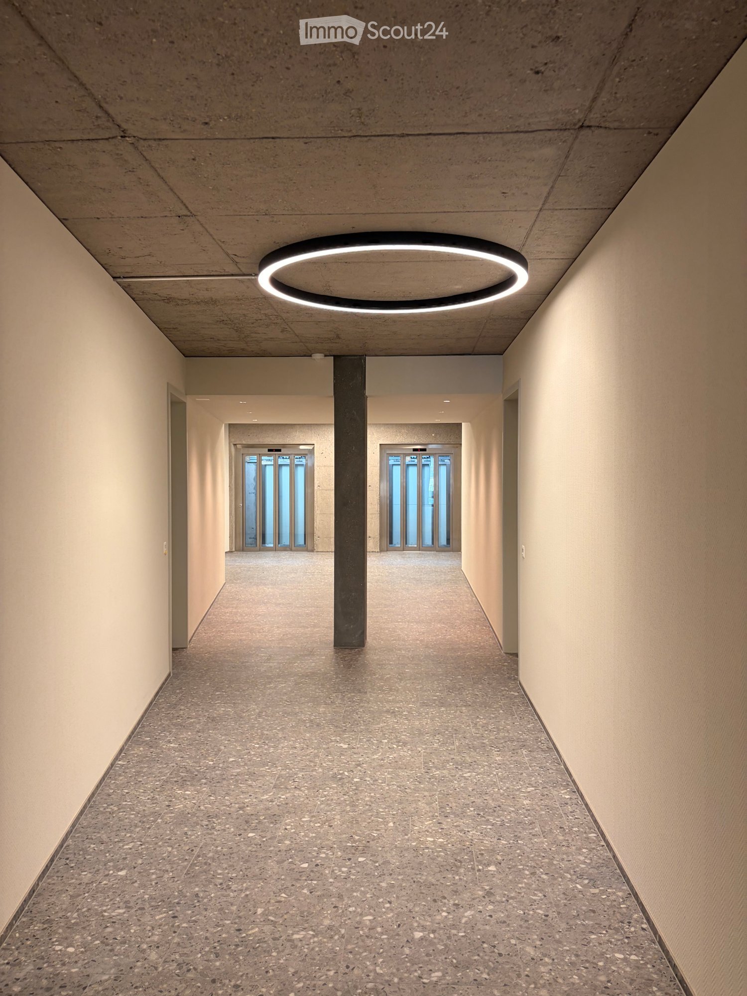 Modern hallway with a circular ceiling light, polished concrete floor, and neutral-colored walls.