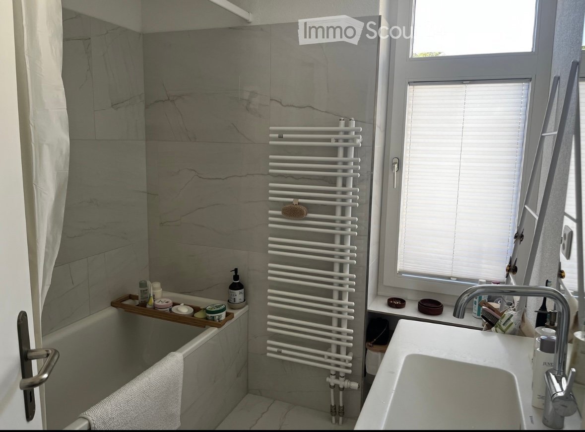 Modern bathroom with marble tiles, a bathtub, a sink, a radiator, and a towel on the edge of the tub.