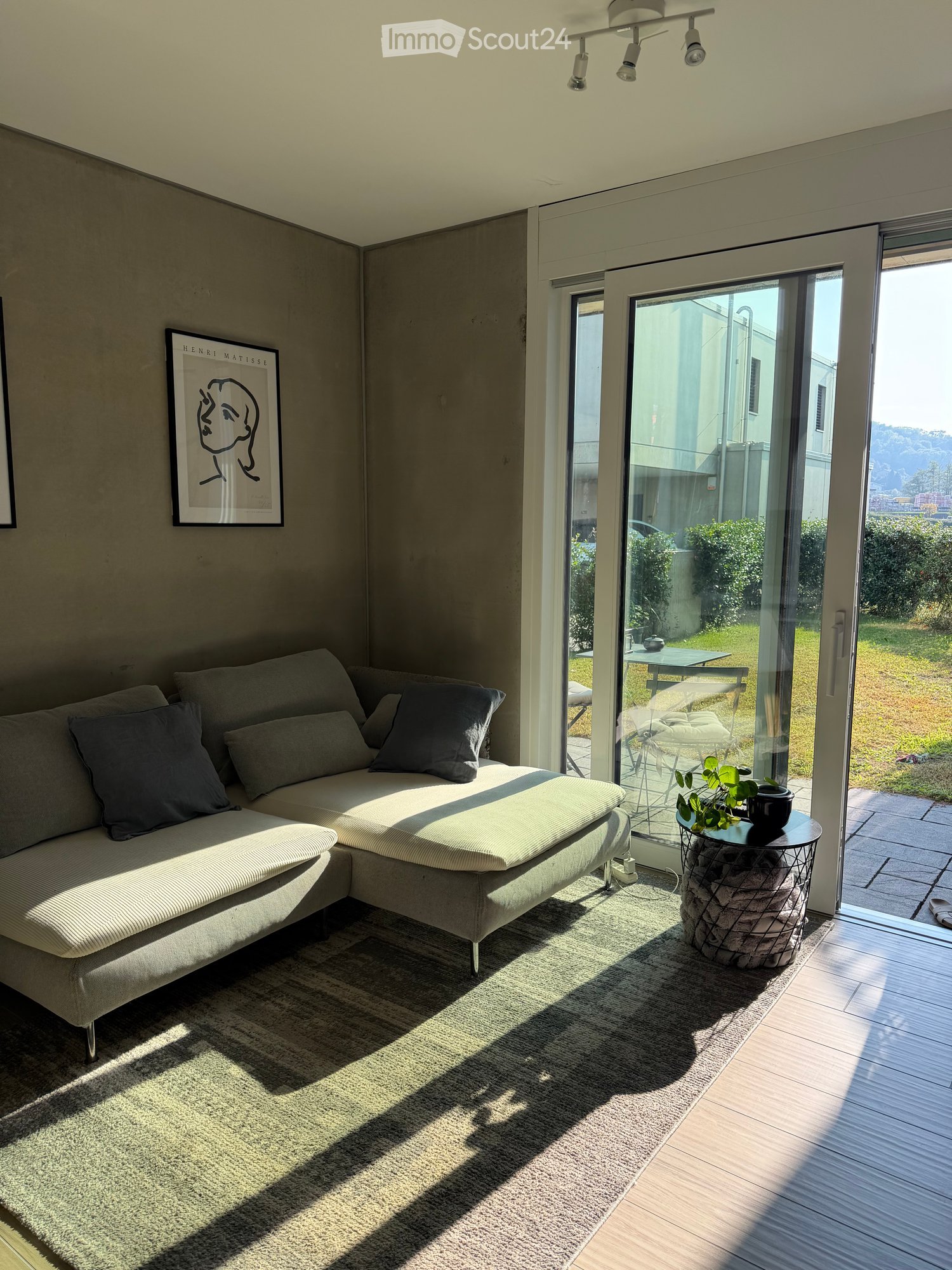 Modern living room with a grey sectional sofa, coffee table, and a view of the garden through large glass doors.