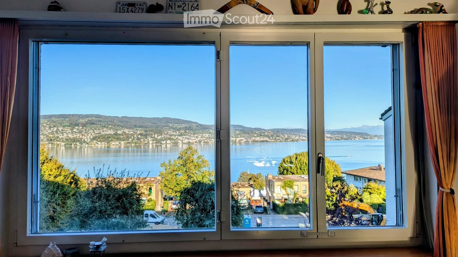 Room with large windows offering a scenic view of a lake and surrounding landscape, with a small table and decorative items on the windowsill.