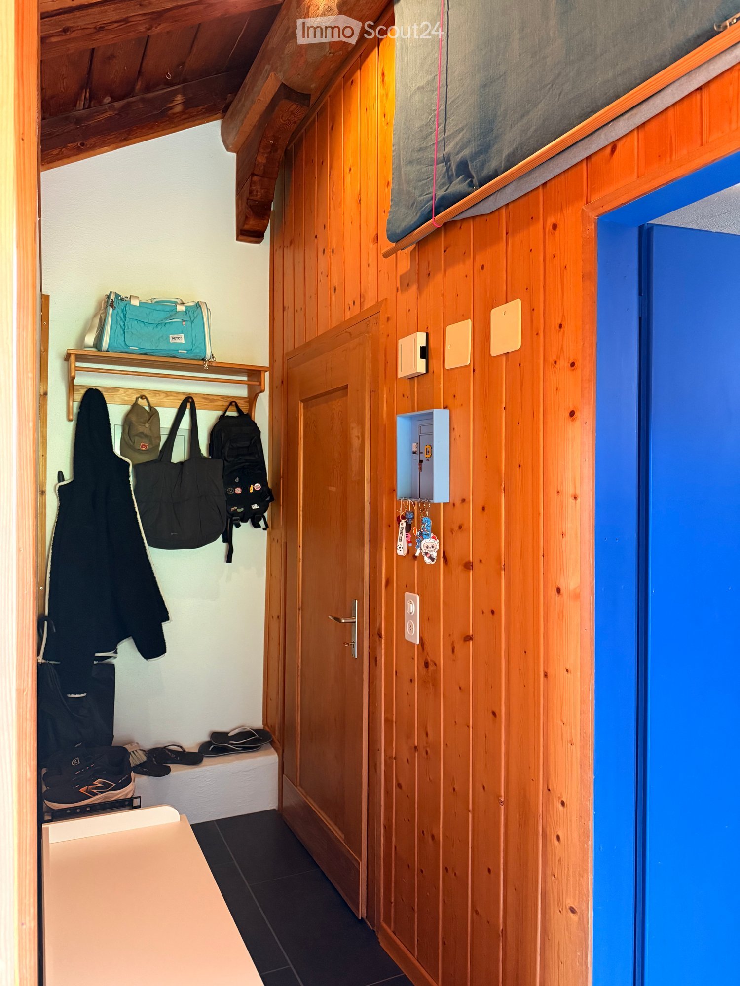 Wooden hallway with coat rack, shelves, and a door leading to another room. Items include jackets, bags, and shoes.