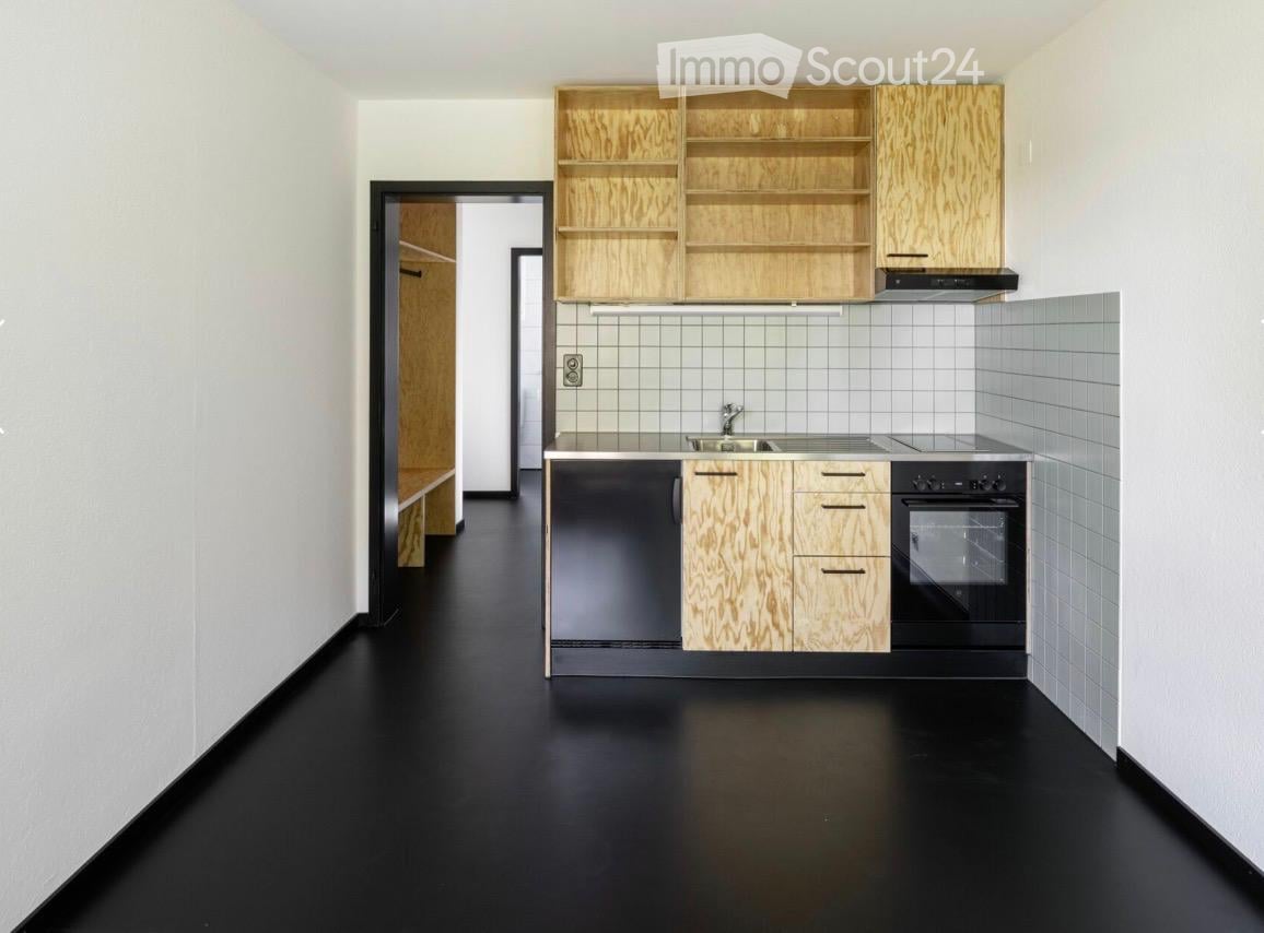 Modern kitchen with black flooring, white tiled backsplash, wooden cabinets, stainless steel sink, and oven.