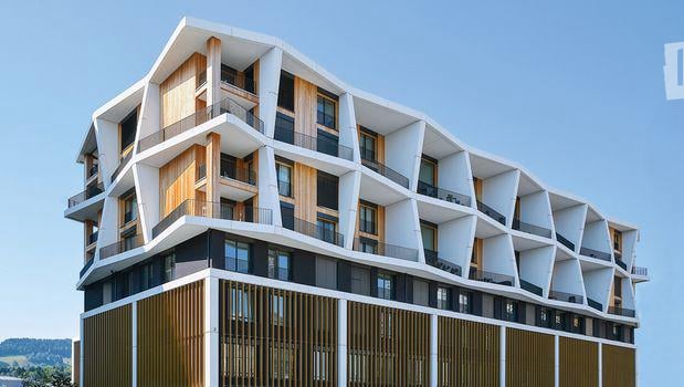 Modern multi-story building with a distinctive geometric facade, featuring balconies and large windows.