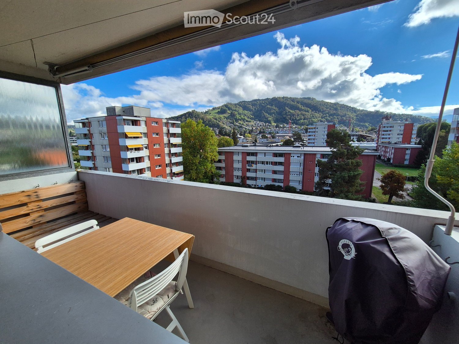 Balcony with wooden table, chairs, bench, and scenic mountain view.
