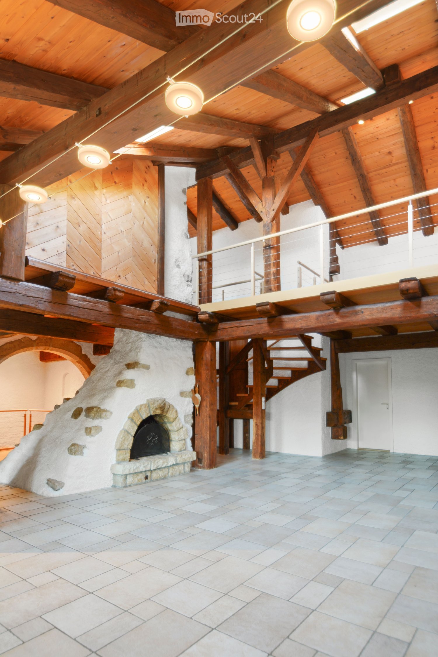Spacious room with exposed wooden beams, a stone fireplace, and a staircase leading to an upper level.