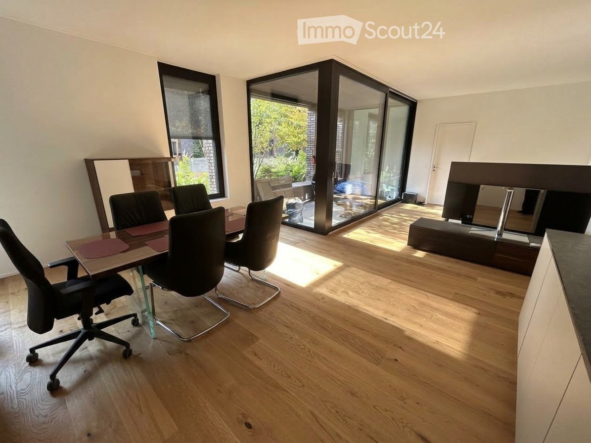 Bright room with wooden flooring, large windows, and sliding glass doors leading to a balcony. Includes a table with chairs and a screen.
